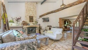 Un vaste espace de vie agrémenté d’une cheminée en pierre, d’un canapé blanc et d’un escalier au style rustique.