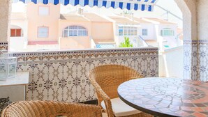 Terraço com móveis de vime e mesa de mosaico, com vista para uma área residencial com azulejos padronizados e edifícios.