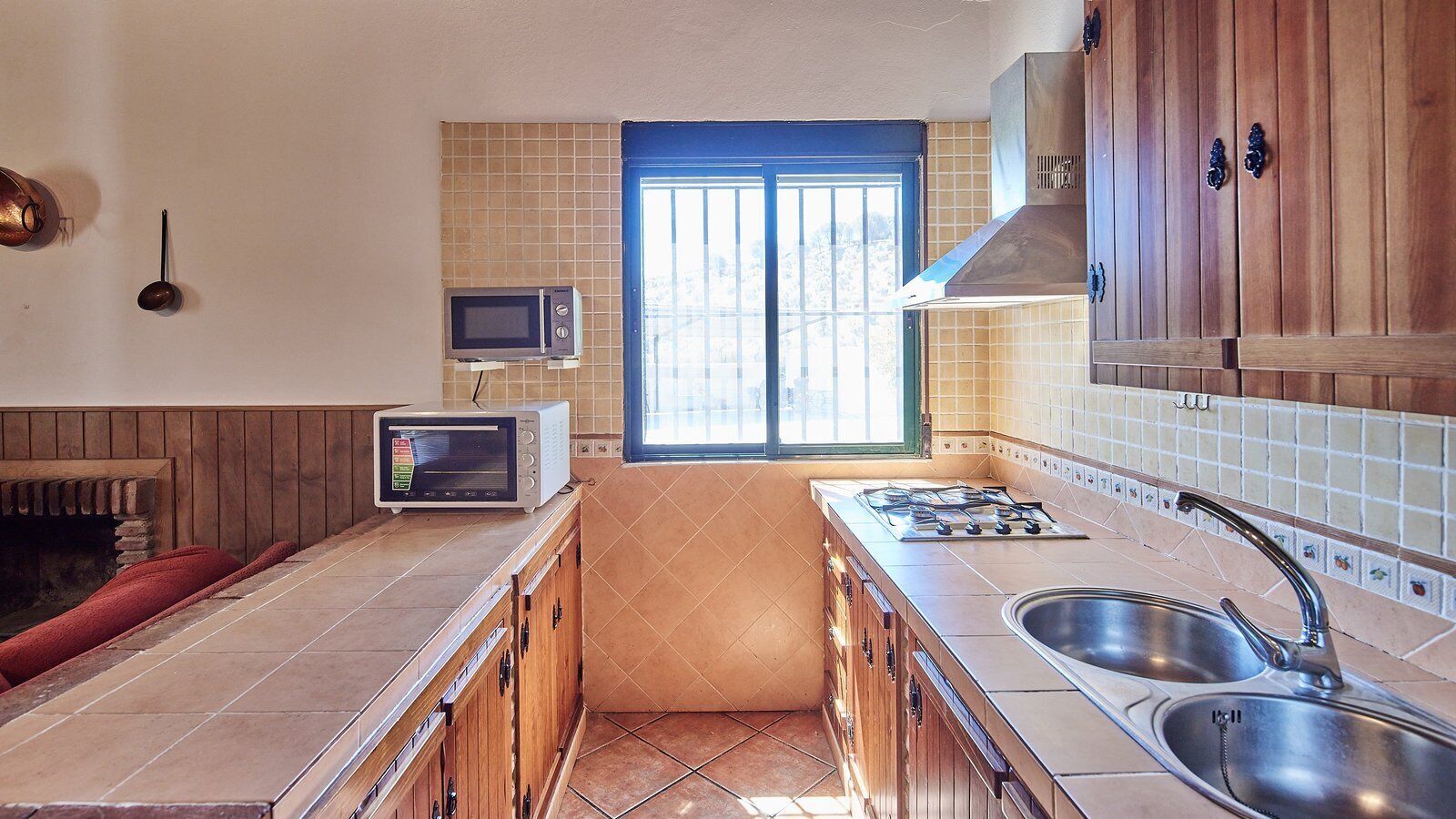 A kitchen with a gas stove, two sinks, a microwave, and a window with a view.