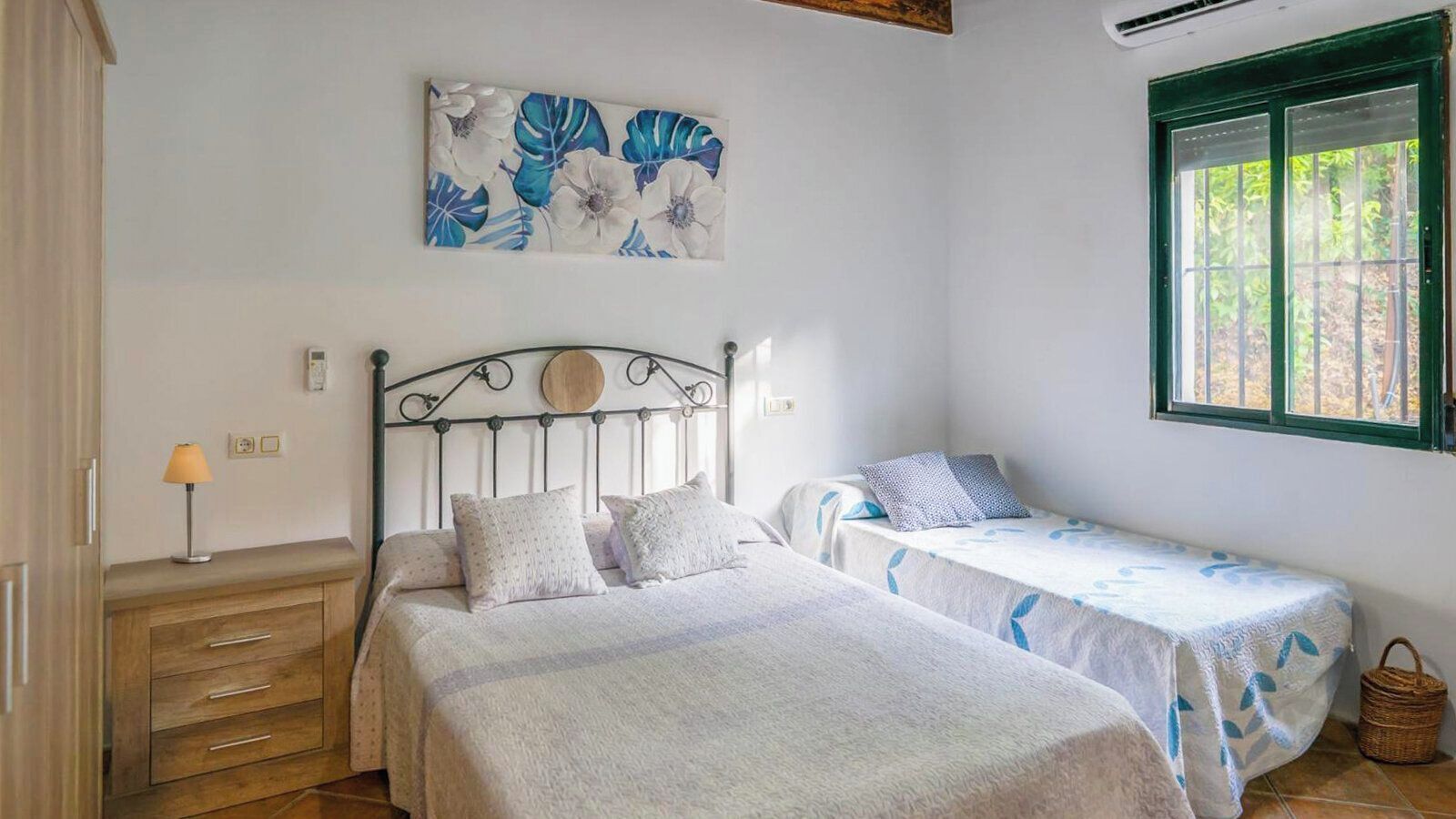 Ein Schlafzimmer mit einem Bett, zwei Nachttischen, einer Lampe, einem Fenster und einem Bild an der Wand.