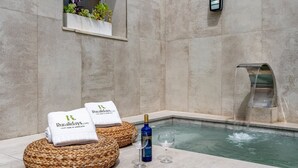 A spa area with a pool, two towels with branding, a bottle of wine, and a wall-mounted water feature. - La Cueva de la Abuela  Cenes de la Vega by Ruralidays (Granada)