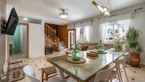 A spacious dining area with a glass table, white chairs, and a large potted plant. - La Cueva de la Abuela  Cenes de la Vega by Ruralidays (Granada)