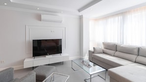 A modern living room with a flat-screen TV on a white console, a grey sofa, and a glass coffee table. - Lux Playa Fuengirola by Ruralidays (Málaga)