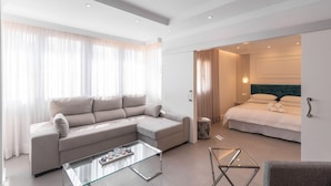 A modern hotel room with a beige sectional sofa, a glass coffee table, a bed with white linens, and a view through an open door. - Lux Playa Fuengirola by Ruralidays (Málaga)