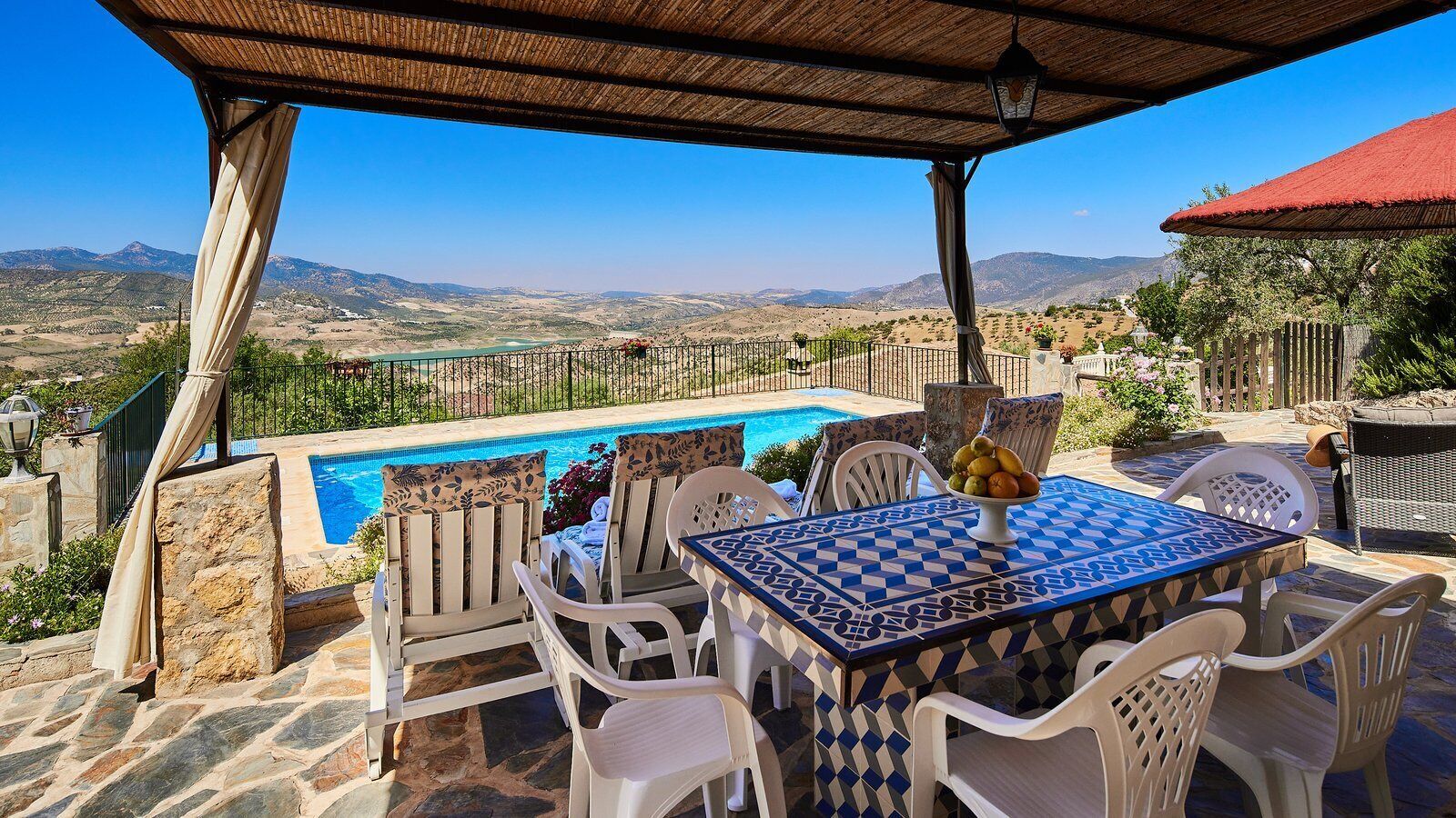 Un área junto a la piscina con mesa y sillas, vistas al paisaje y una pérgola.