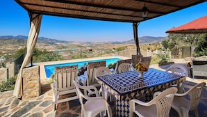 Ein Poolbereich mit Tisch und Stühlen, Blick auf die Landschaft und einer Pergola.