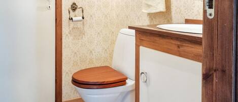 Un baño con inodoro, tocador de madera, toalla colgada en un perchero y puerta con cerradura.