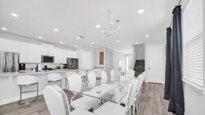 A modern kitchen with white cabinets, stainless steel appliances, and a glass dining table with white chairs. - Modern Family Villa With Private Pool and Hot Tub (Reunion)