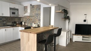 A modern kitchen with white cabinets, a wooden island with bar stools, a built-in microwave, and a patterned backsplash. - Vila Luisa Anabela 6/8 Personnes Piscine et Jacuzzi (Albufeira)