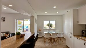 A modern kitchen with white cabinets, a wooden dining table, and a glass-top dining table. - Vila Luisa Anabela 6/8 Personnes Piscine et Jacuzzi (Albufeira)