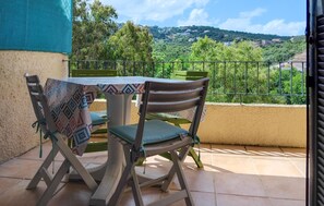 A balcony with a table and chairs, a view of a hillside, and a metal railing.