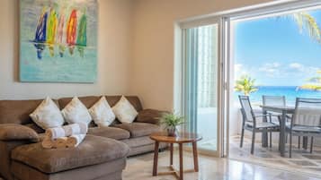 Un salón con sofá, almohadones, una mesita con una planta y vista al océano a través de un ventanal.