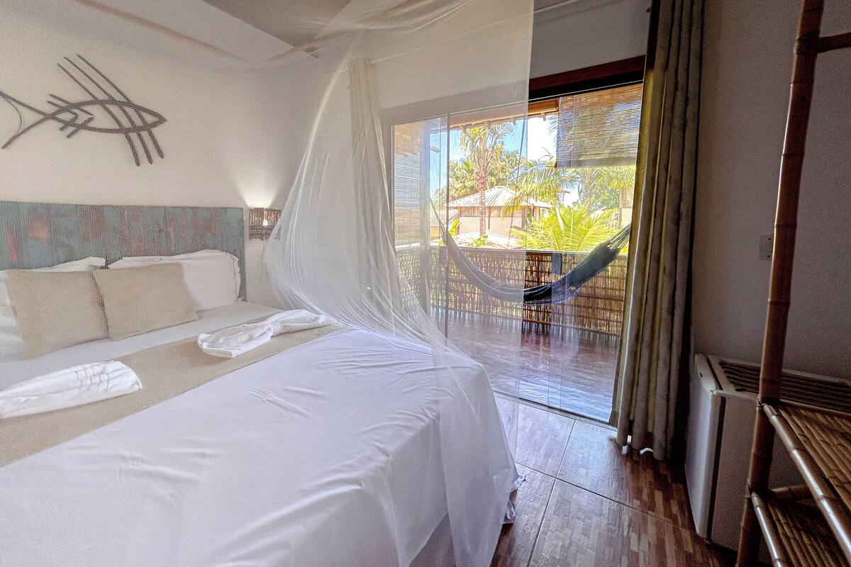 A bedroom with a bed, a hammock, and a view of the outdoors.