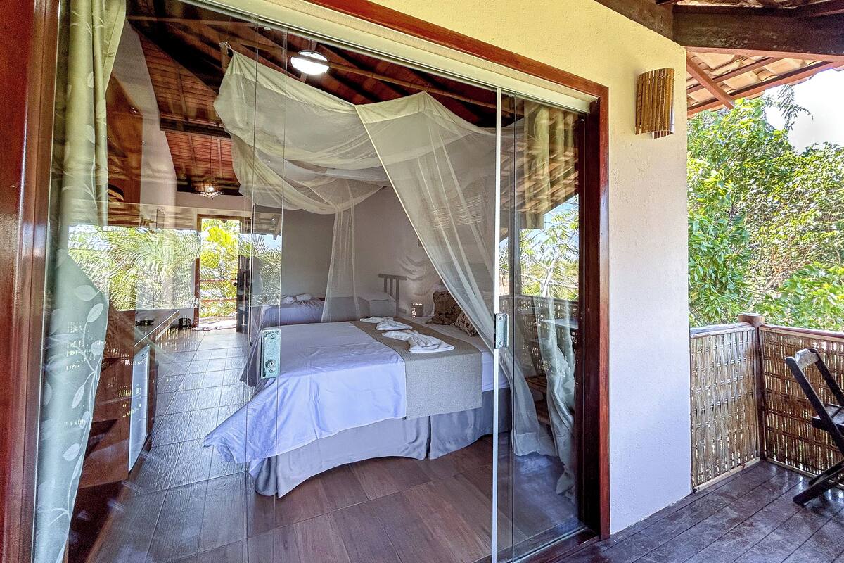 A bedroom with a glass door, a bed, and a view of greenery outside.