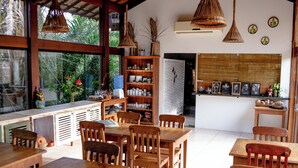Un restaurant avec des tables et des chaises en bois, une grande fenêtre donnant sur un paysage verdoyant et un mur décoré de tableaux encadrés.