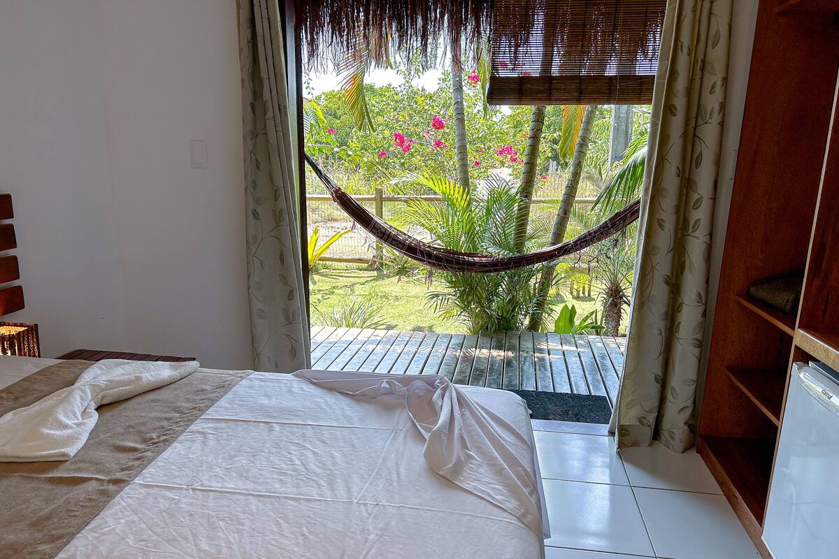 A bedroom with a bed, a view of a garden through a window, and a hammock.