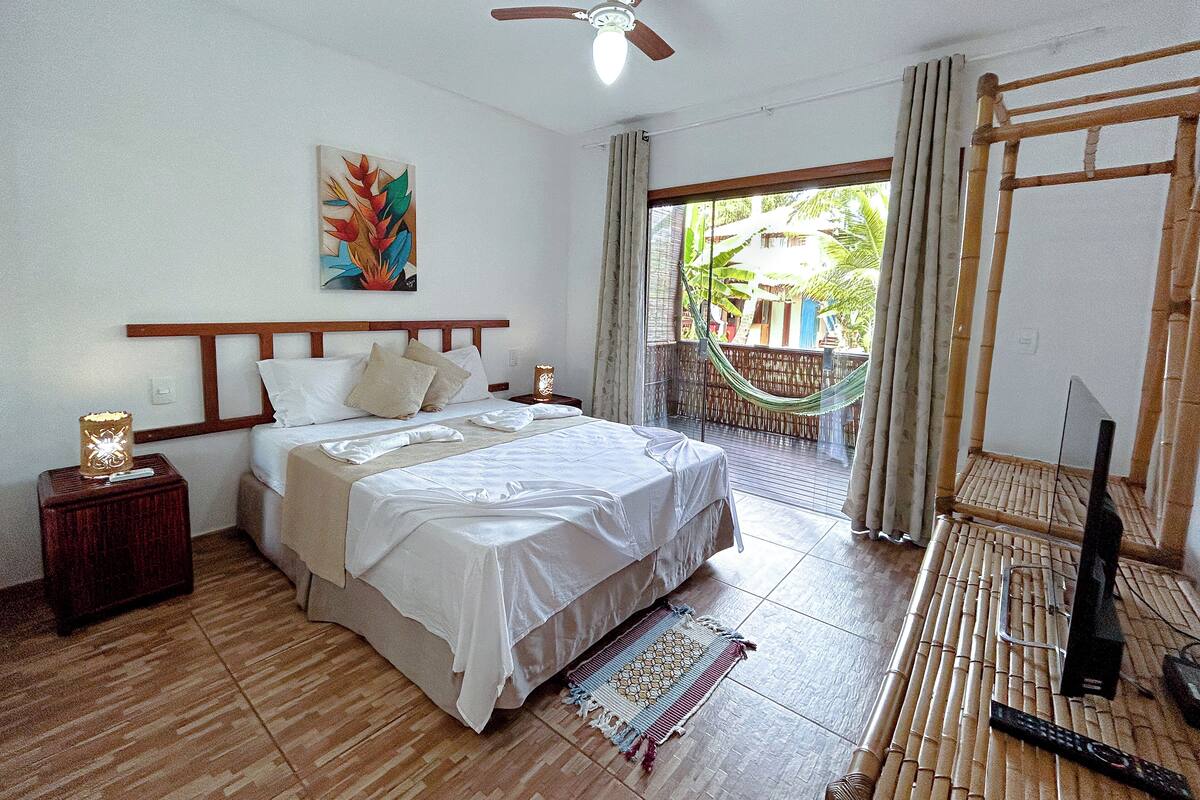 A bedroom with a bed, a ceiling fan, a hammock, and a view of the outdoors.