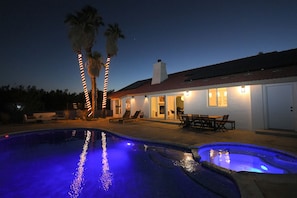 Ein Swimmingpool mit blauem Licht, Palmen und einem Haus mit Außensitzgelegenheiten.
