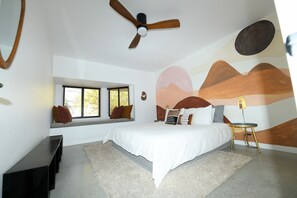 A bedroom with a large bed, a ceiling fan, a window with a view, and a wall mural. - Design newly remodeled  villa. 10 minutes from Palm Springs (Desert Hot Springs)