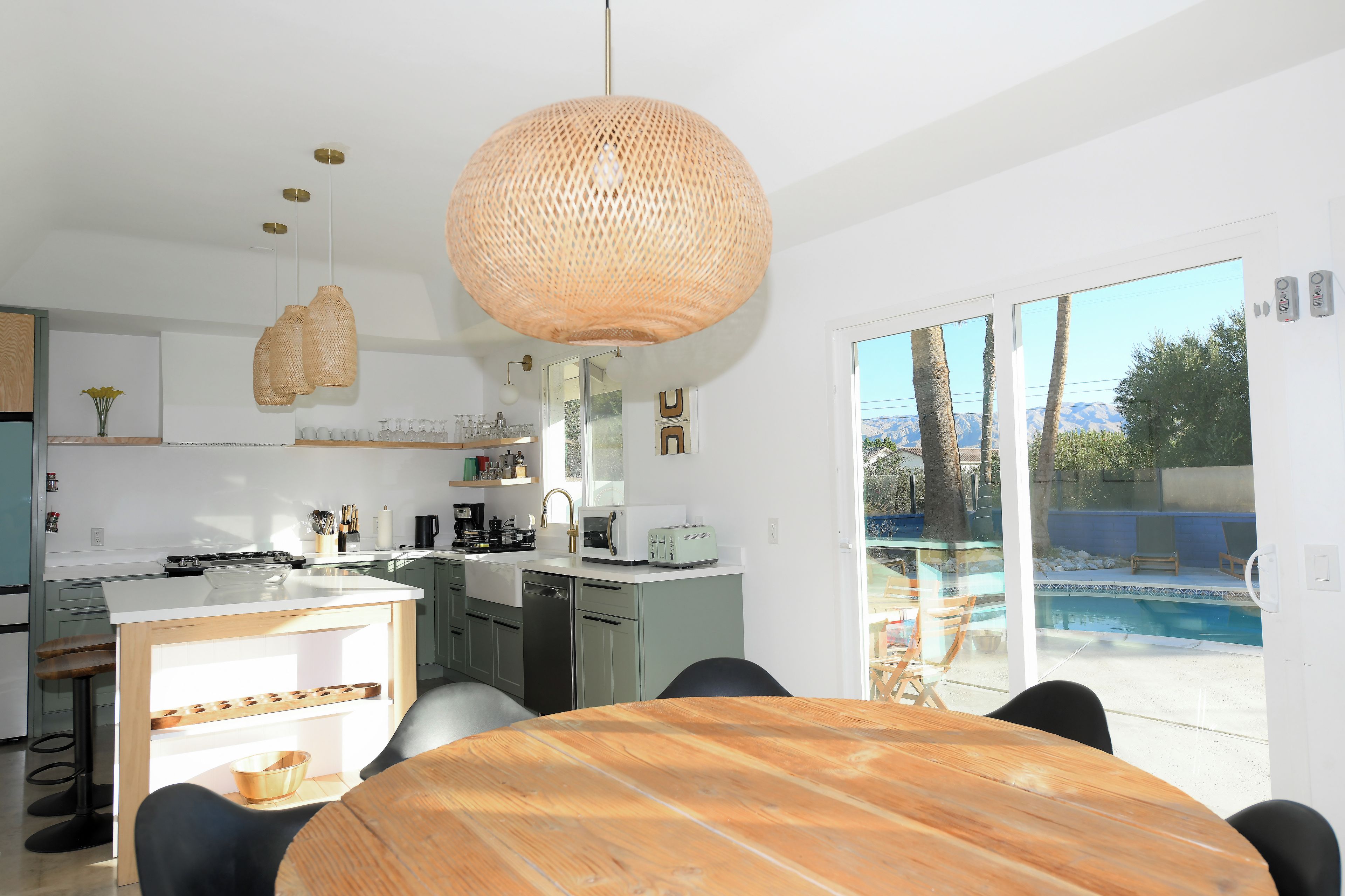 A modern kitchen with a dining area, a large woven light fixture, and a view of a swimming pool.