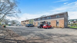 Un parking avec plusieurs voitures, un bâtiment doté de nombreuses fenêtres et un ciel dégagé.