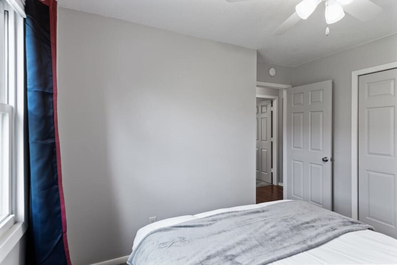 A bedroom with a bed, a window with curtains, and a door leading to another room.