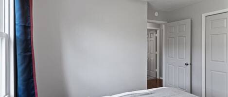 A bedroom with a bed, a window with curtains, and a door leading to another room.