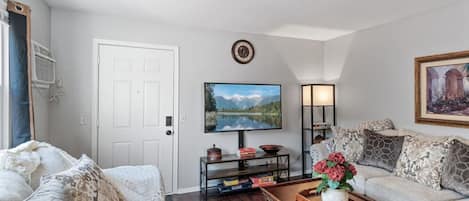 A living room with a sofa, a coffee table with a plant, a TV, and a bookshelf.