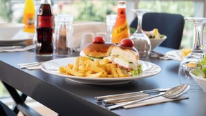Ett bord dukat med en smörgås, pommes frites och olika tillbehör i ett ljust rum med stora fönster.