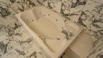 Una bañera rectangular con un solo grifo y un cabezal de ducha manual, frente a un fondo de azulejos de mármol.
