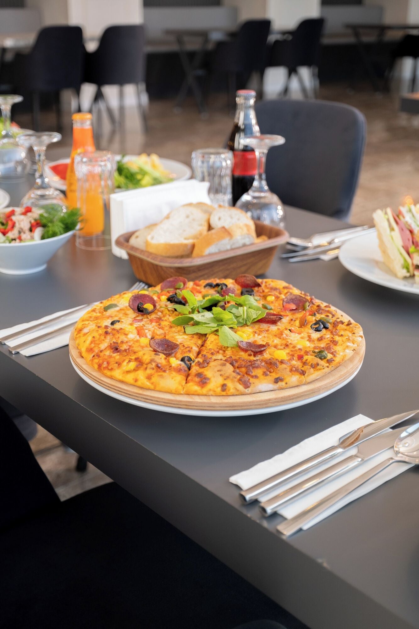 Pizza sobre uma mesa com acompanhamentos e bebidas.