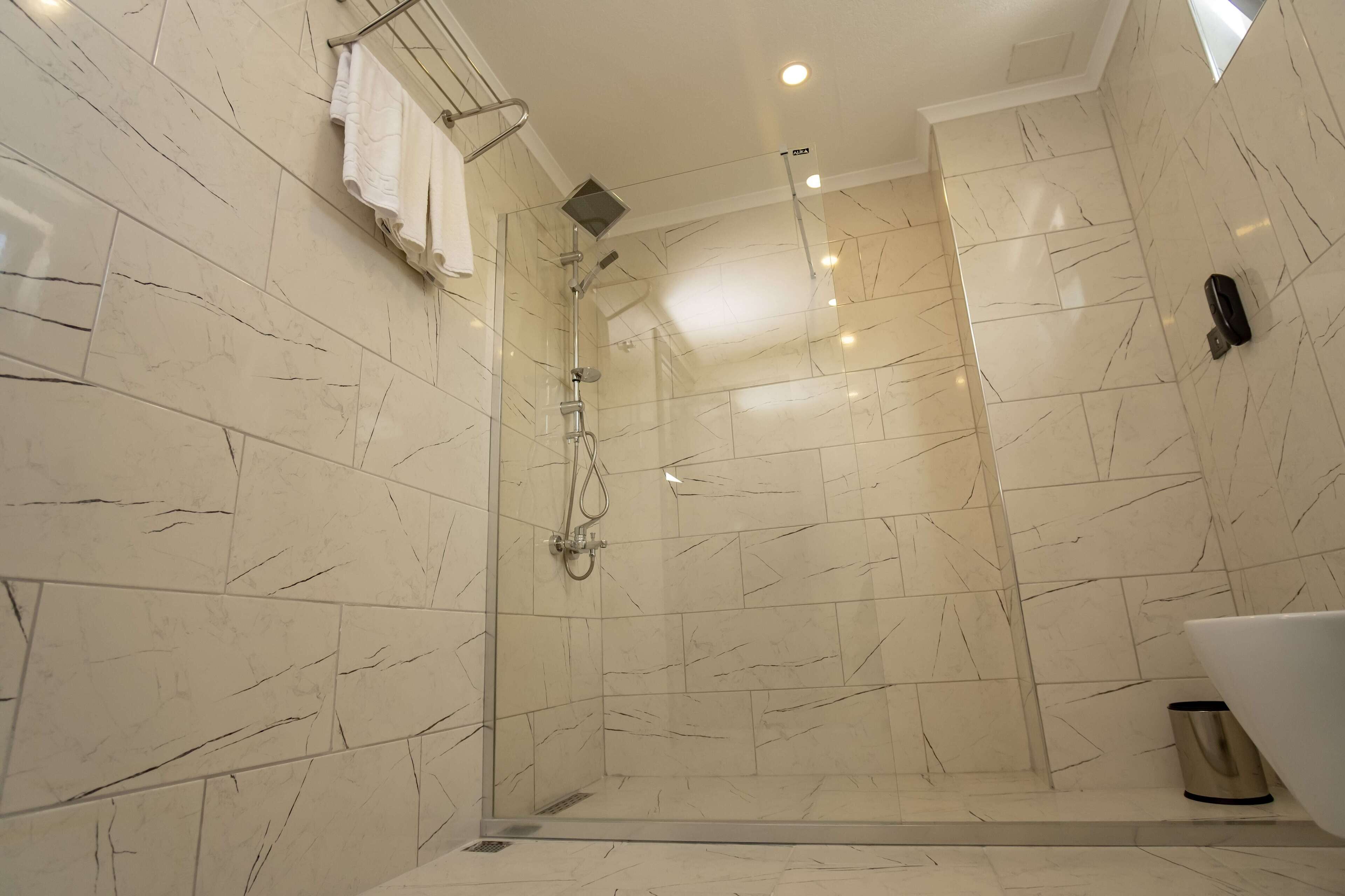 A modern bathroom with a glass-enclosed shower, marble walls, and a white bathtub.