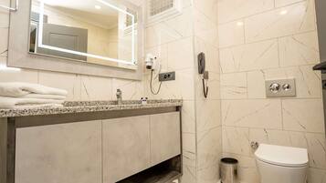 A modern bathroom with a marble-tiled wall, a vanity with a sink, a hairdryer, a telephone, and a toilet.
