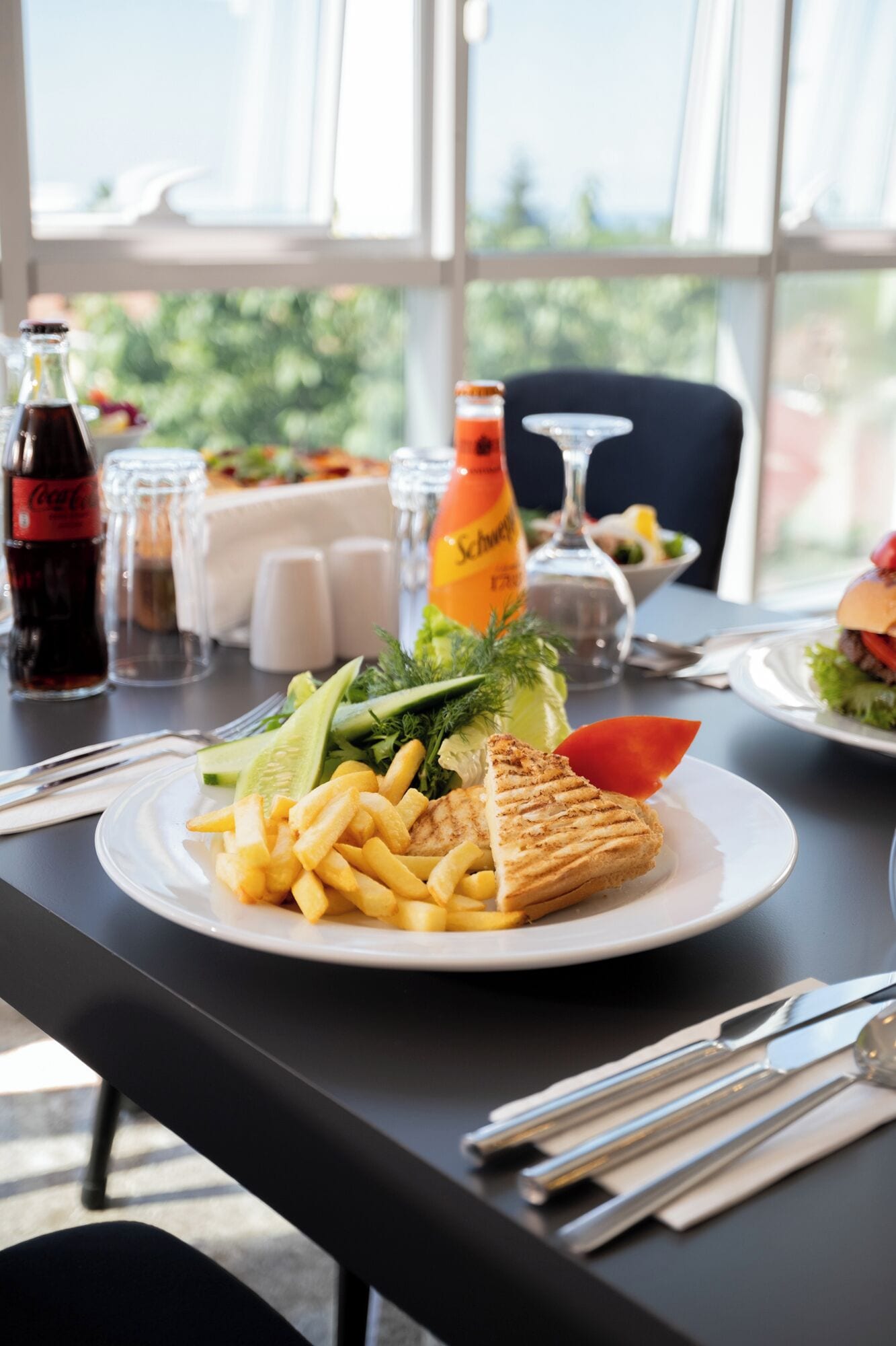 A dining table with a plate of food, including a sandwich, fries, and vegetables. There are drinks and glasses on the table.