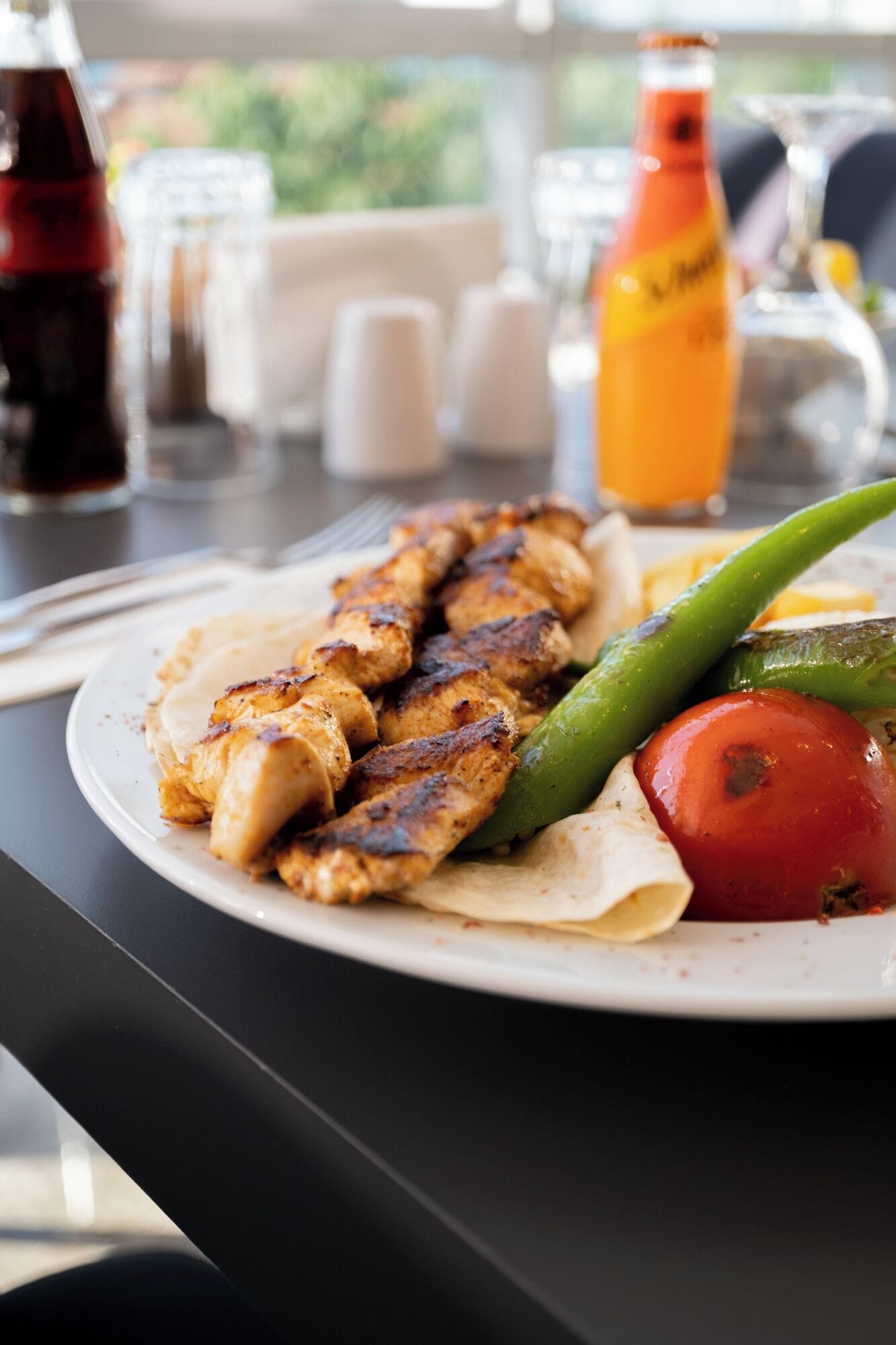 A plate of grilled chicken skewers with vegetables on a table.
