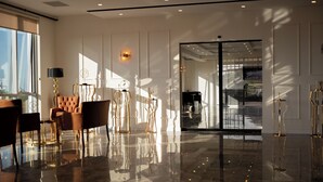 En rymlig entréhall med ett reflekterande golv, en sittgrupp med en soffa och stolar samt en stor glasdörr som leder till ett annat rum.