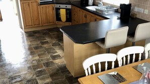 A kitchen with wooden cabinets, a black countertop, a stove, and a dining area with a table and chairs. - Cleomack House
Home from Home @Mourne Mountains  (Hilltown)