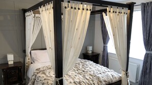 A four-poster bed with white and grey curtains, a fluffy white and grey blanket, and a wooden nightstand with a lamp. - Cleomack House
Home from Home @Mourne Mountains  (Hilltown)