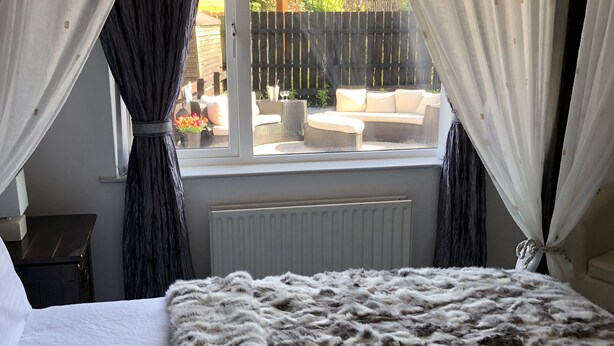 A bedroom with a large bed, white curtains, and a view of an outdoor patio area. - Cleomack House
Home from Home @Mourne Mountains  (Hilltown)