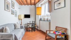 Un salon comprenant un canapé, une chaise en bois, un téléviseur, une table avec une lampe et une fenêtre avec des rideaux.