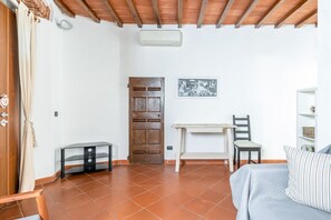 Una habitación con puerta de madera, una mesita, una silla, una cama y aire acondicionado de pared.