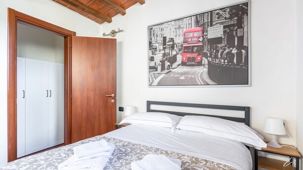 Une chambre à coucher avec un lit, une armoire en bois, une photographie encadrée représentant une rue de la ville, et une table de chevet avec une lampe.