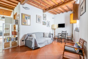Una sala de estar con un sofá, una televisión, una mesa, sillas y una estantería.