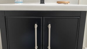 Ein schwarzes Schränkchen mit zwei Türen, einer weißen Arbeitsplatte, einem Seifenspender und einem Wasserhahn.