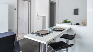 Une cuisine moderne avec un plan de travail blanc, deux tabourets de bar noirs, un meuble blanc et une porte dotée d ’un panneau en verre dépoli.