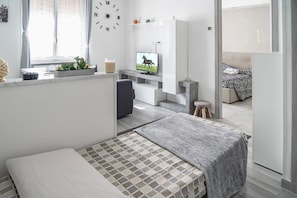 Una habitación moderna y bien iluminada con una cama, un televisor, un escritorio y un sofá.