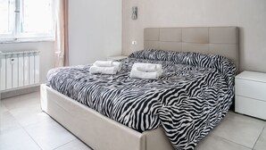 Une chambre à coucher avec une couvre-lit à motifs zébrés, une table de chevet blanche, un radiateur et une fenêtre avec des rideaux.