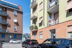 Un edificio residencial de varios pisos con balcones, zona de estacionamiento y cielo azul despejado.