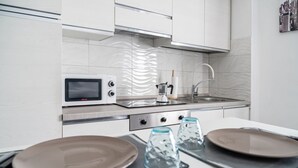 Une cuisine moderne avec des meubles blancs, un four à micro-ondes, une bouilloire et un évier.