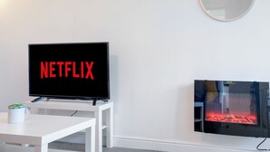 A modern living room with a flat-screen TV displaying the Netflix logo, a fireplace, and a round mirror on the wall. - 2 bed luxury apartment (Enfield)